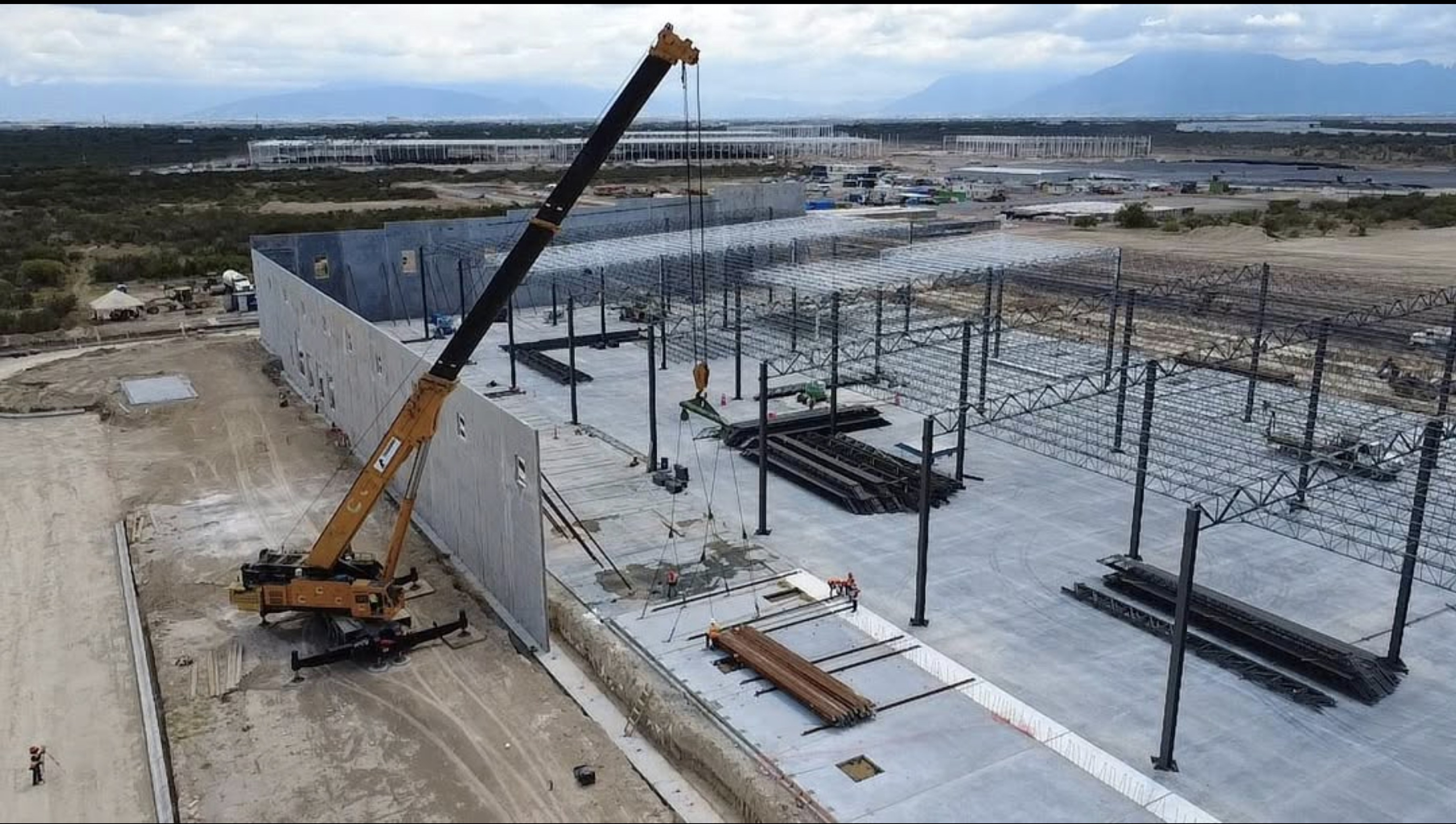 Grúa izando panel de concreto sobre losa de nave industrial